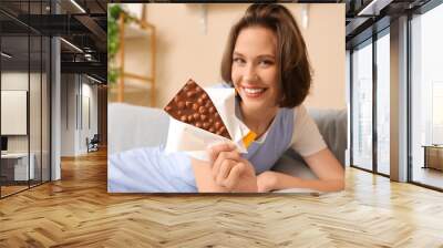 Beautiful young happy woman with tasty chocolate bar at home Wall mural