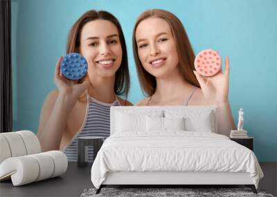 Beautiful young sisters with hair scalp massagers on blue background Wall mural