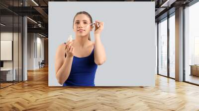 Beautiful young woman applying cosmetic serum on her face against grey background Wall mural