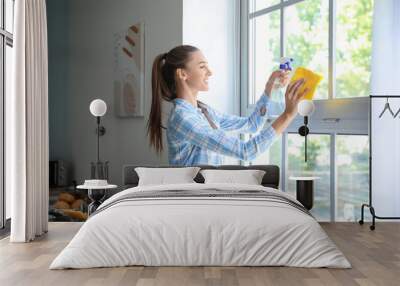 Beautiful young woman cleaning window at home Wall mural