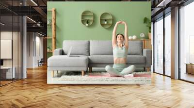 Beautiful young woman doing yoga on mat in living room Wall mural