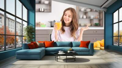 Beautiful young woman drinking orange juice in kitchen Wall mural