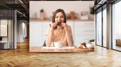 Beautiful young woman eating tasty chocolate at home Wall mural