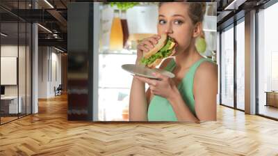 Beautiful young woman eating unhealthy food near refrigerator at night Wall mural