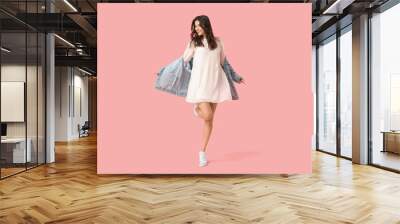 beautiful young woman in stylish white dress and denim jacket dancing on pink background Wall mural