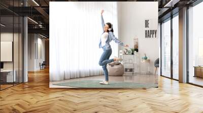 Beautiful young woman listening to music and dancing at home Wall mural