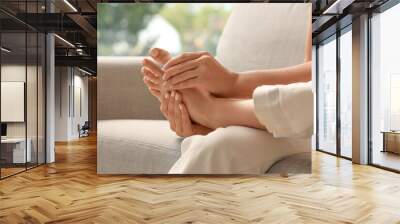 Beautiful young woman making foot massage on sofa in living room at home Wall mural