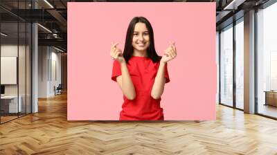 Beautiful young woman making hearts with fingers on pink background Wall mural