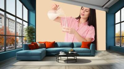 Beautiful young woman pouring milk into glass on beige background Wall mural