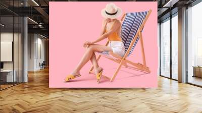 Beautiful young woman relaxing on deck chair against pink background Wall mural