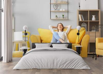 Beautiful young woman relaxing on sofa in living room Wall mural