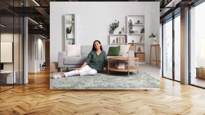 Beautiful young woman sitting on floor in living room Wall mural