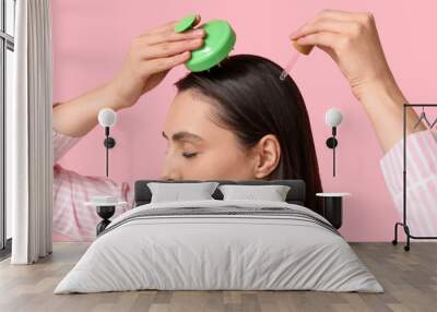 Beautiful young woman using hair scalp massager and cosmetic oil on pink background Wall mural