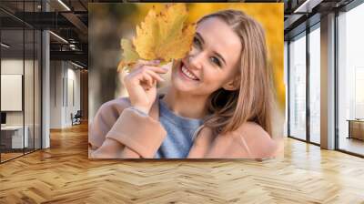 Beautiful young woman with autumn leaves in park Wall mural