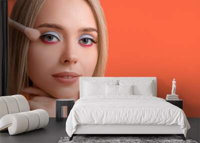 Beautiful young woman with brush applying colorful eyeshadows on orange background Wall mural