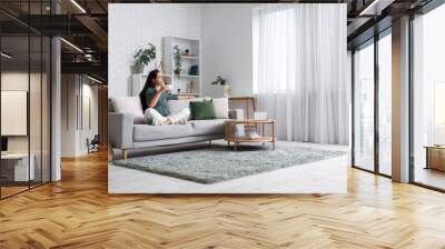 Beautiful young woman with cup of coffee sitting on sofa in living room Wall mural