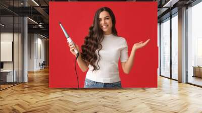 Beautiful young woman with curling iron on red background Wall mural