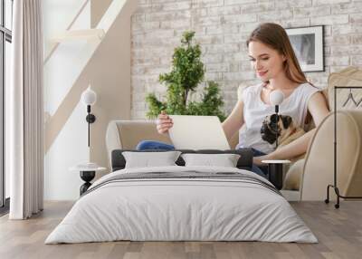 Beautiful young woman with cute pug dog working on laptop at home Wall mural