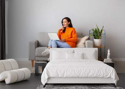 Beautiful young woman with laptop resting on couch at home Wall mural