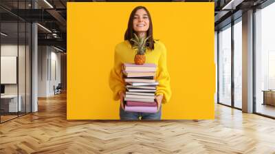 Beautiful young woman with many books and pineapple on yellow background Wall mural