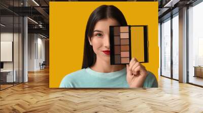 Beautiful young woman with palette of eyeshadows on yellow background Wall mural