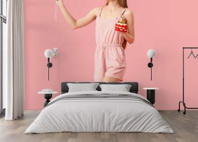 Beautiful young woman with tasty birthday cake and balloons on pink background Wall mural