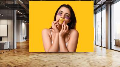 Beautiful young woman with under-eye patches and lip mask on yellow background Wall mural