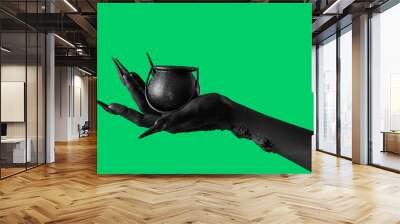 Black hand of witch with cauldron on green background. Halloween celebration Wall mural