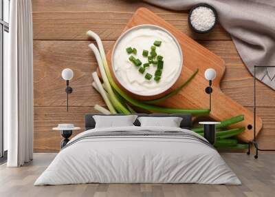 Board and bowl of tasty sour cream with green onion on wooden background Wall mural