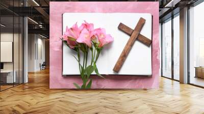 Book with lily flowers and wooden cross on pink background Wall mural