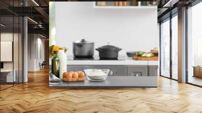 Bowl with flour, eggs and bottle of milk on table in modern kitchen Wall mural