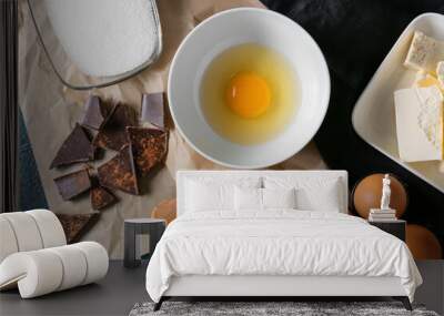 Bowl with fresh egg and ingredients for preparing chocolate brownie on black background Wall mural