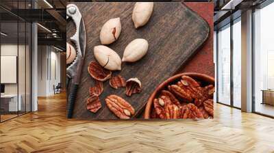 Bowl with tasty pecan nuts, nutcracker and board on dark background Wall mural