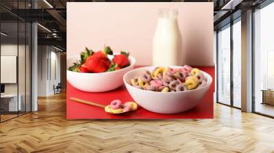 Bowls with colorful sweet cereal rings, strawberries and bottle of milk on red table Wall mural