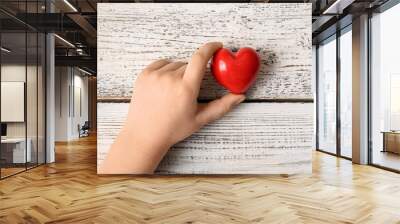 Child's hand with red heart on light wooden background Wall mural