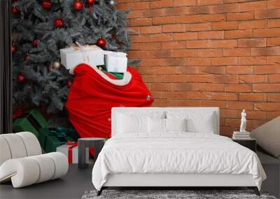 Christmas tree with gifts and Santa bag near brick wall in room Wall mural