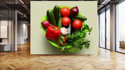 Colander with fresh vegetables and greenery on light green background Wall mural