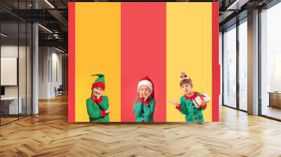 Collage of little children in elf costumes on yellow and red backgrounds. Christmas celebration Wall mural