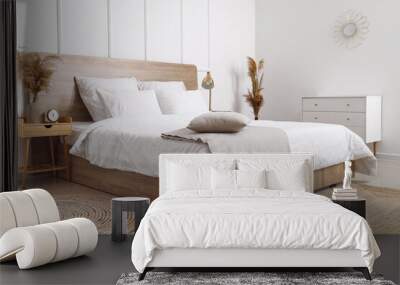 Comfortable bed, dry reeds and chest of drawers near white wall Wall mural