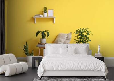 Comfortable bench, shelf, pillows and houseplants near yellow wall in beautiful room Wall mural