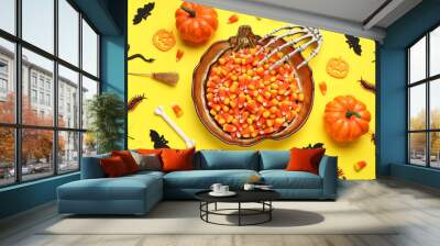 Composition with plate of tasty candy corns and different Halloween decorations on yellow background Wall mural