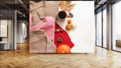 Composition with stylish female sweaters, cup of coffee and autumn decor on light background Wall mural