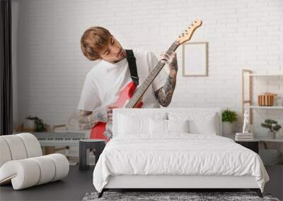 Cool tattooed young man playing electric guitar at home Wall mural