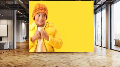 Cute African-American boy in warm winter clothes on yellow background with space for text Wall mural