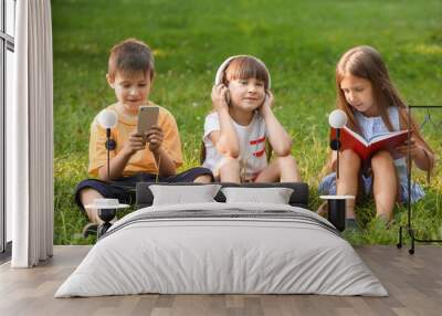 Cute little children reading book and listening to music in park on summer day Wall mural