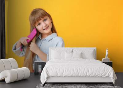 Cute little girl brushing hair on color background Wall mural