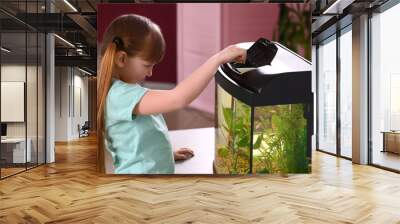 Cute little girl feeding fish in aquarium Wall mural