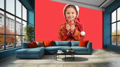 Cute little girl in Santa hat with candy canes on red background Wall mural