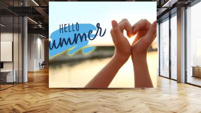 Cute little girl making heart with her hands outdoors at sunset. Hello, summer Wall mural