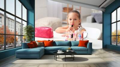 Cute little girl with cosmetic bag and different makeup products at table in living room Wall mural